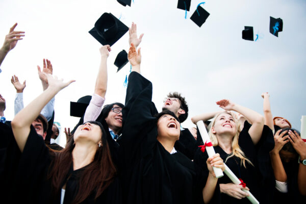 group diverse grads throwing caps up sky